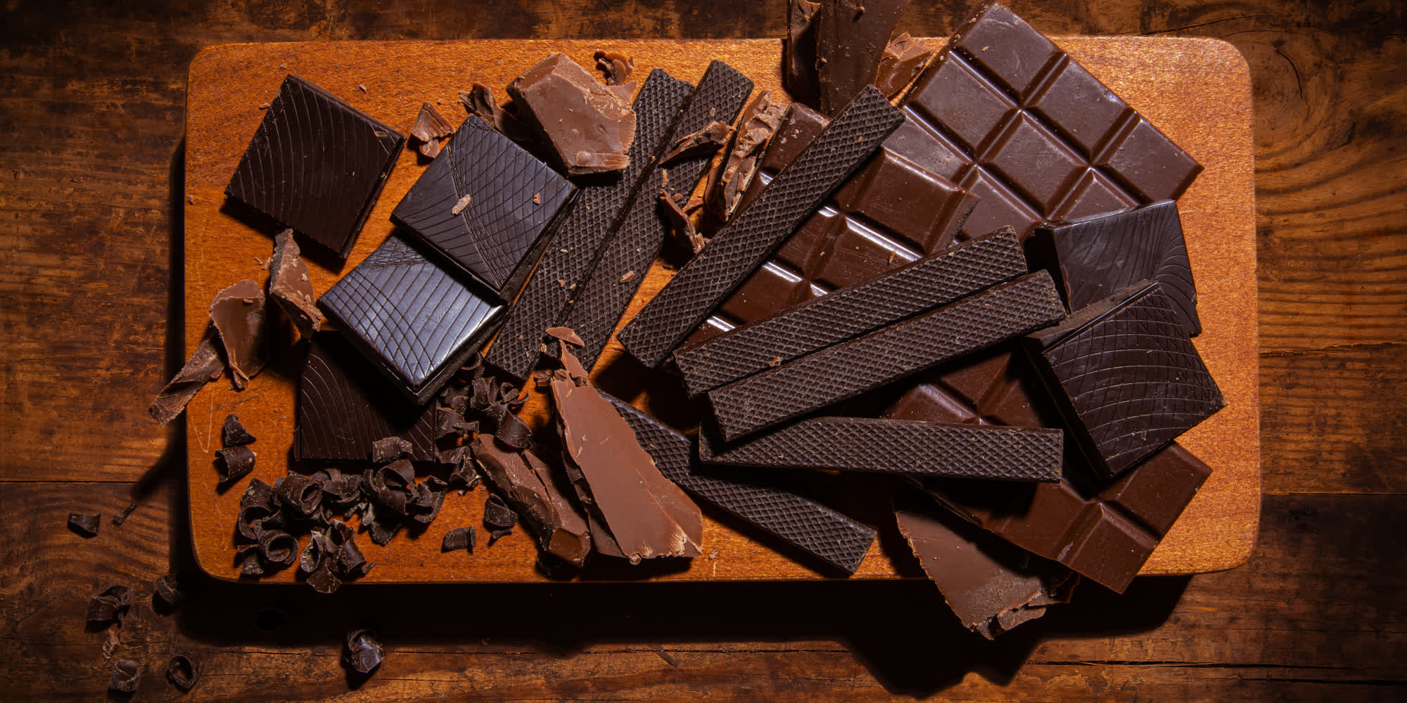 Broken dark chocolate bars and cacao nibs arranged on a wooden board
